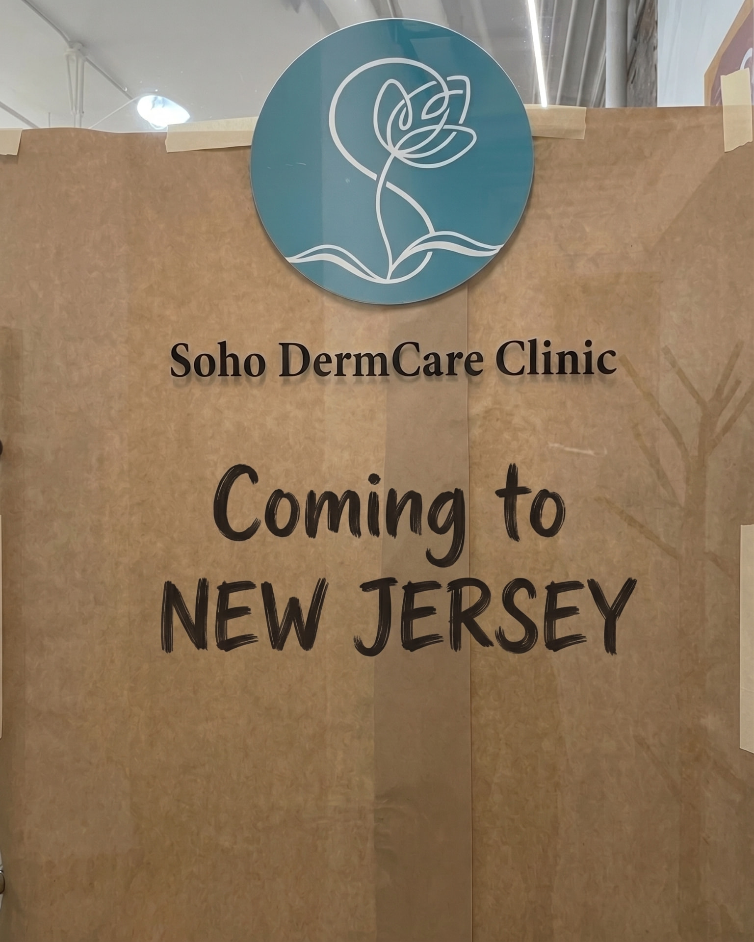 Construction-wrapped storefront with the Soho DermCare Clinic sign above handwritten marker text reading "Coming to New Jersey"